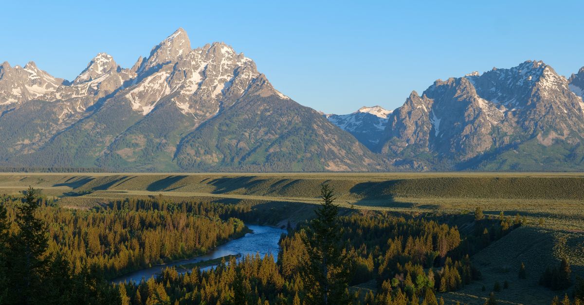 Experience the stunning Grand Teton mountains with vibrant greenery and a serene river at sunrise in Wyoming.